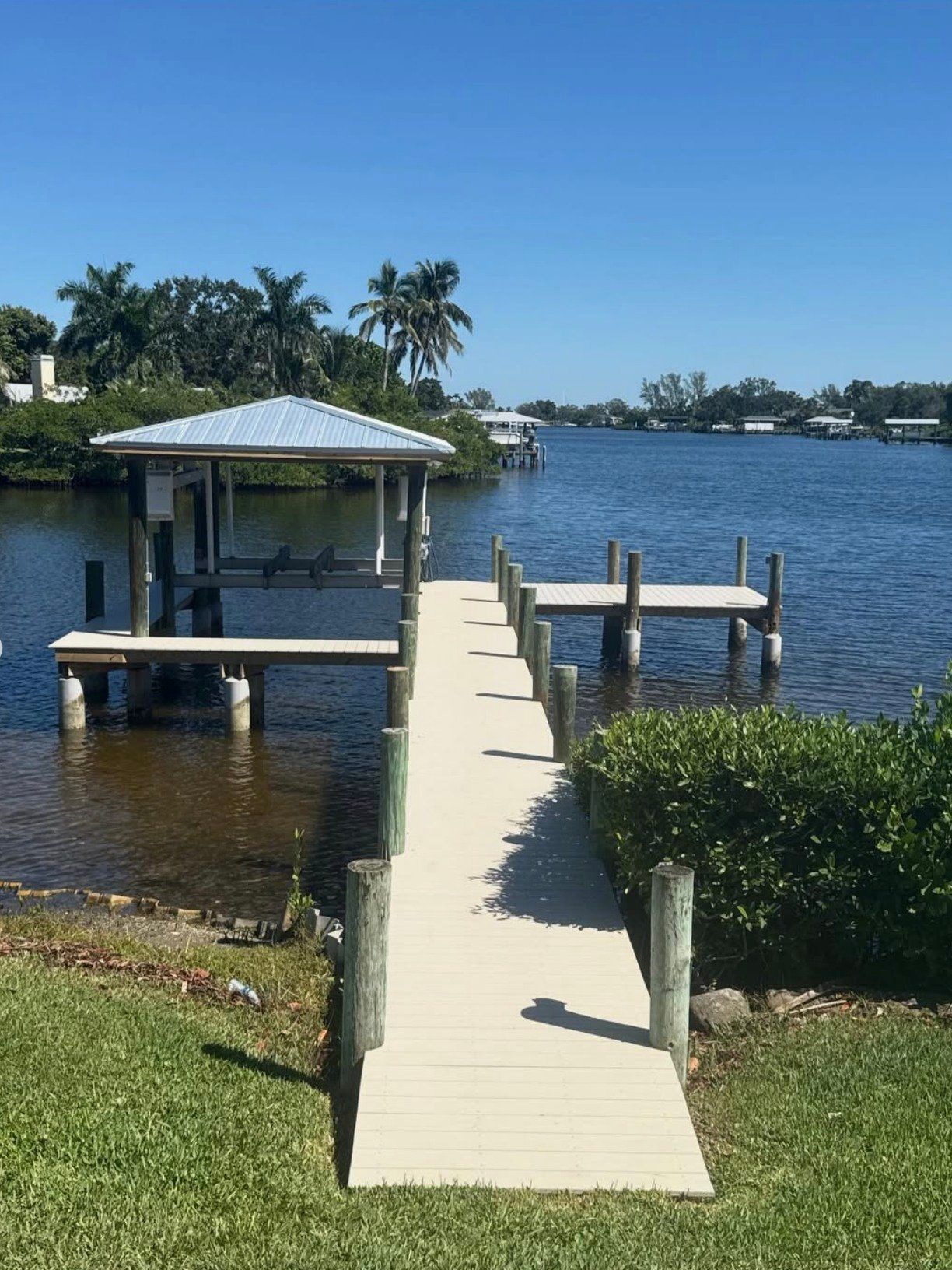 A wooden dock with a covered boat slip extending into a calm blue river on a sunny day.