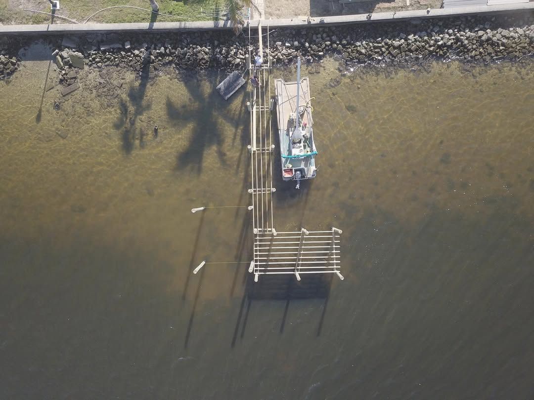 Aerial view of a small boat docked at a wooden pier beside a shoreline and calm water.