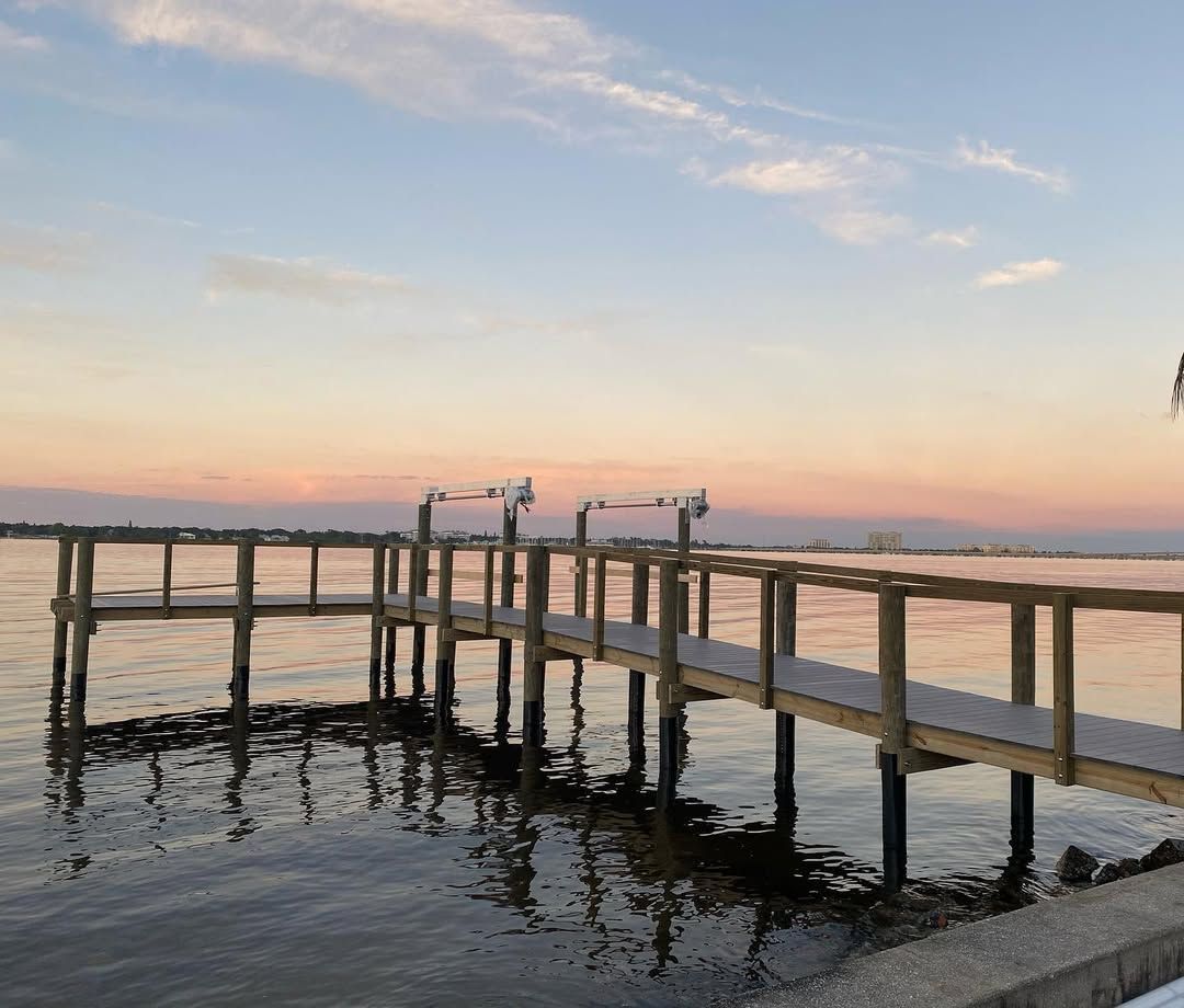Wooden dock over calm water at sunset with pink and blue sky.