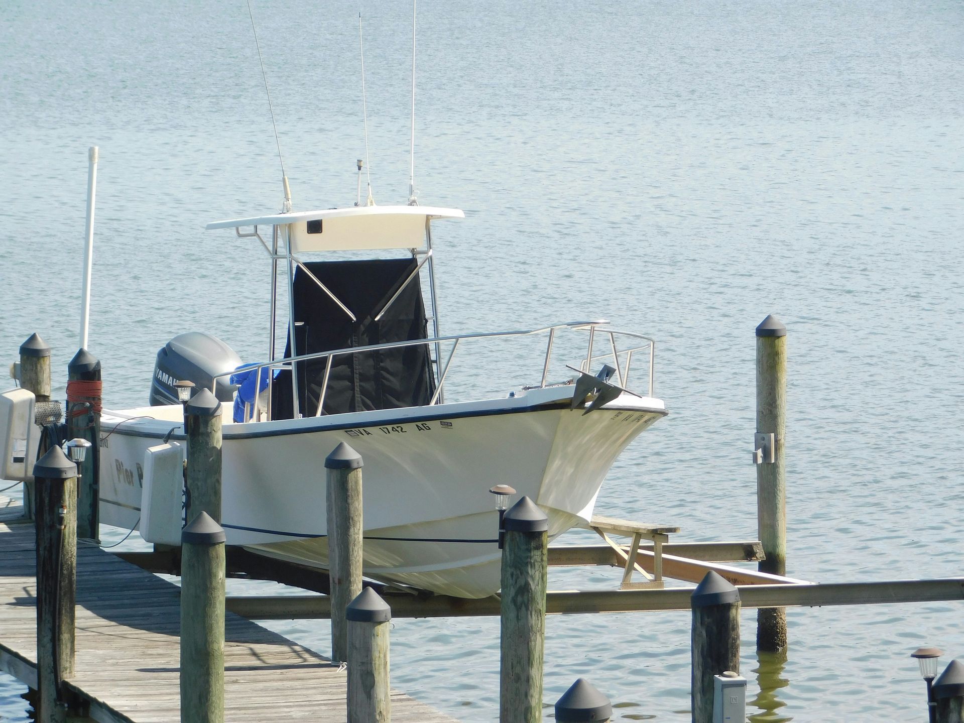 A white center console fishing boat moored at a wooden dock on calm water.