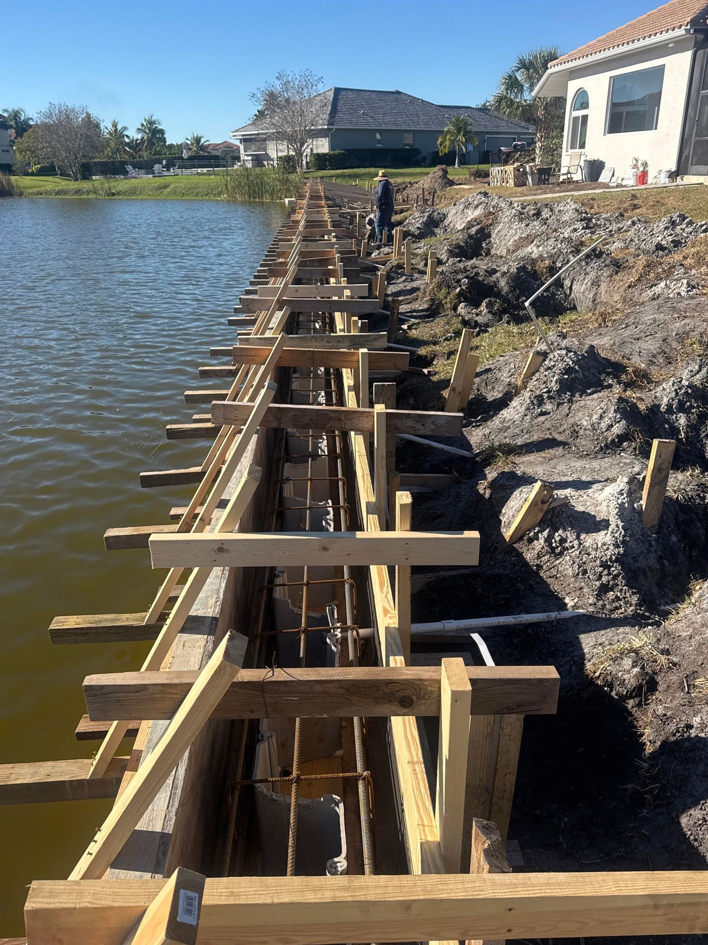 Wooden forms and metal rebar installed for a concrete seawall construction project along a residential lakefront.