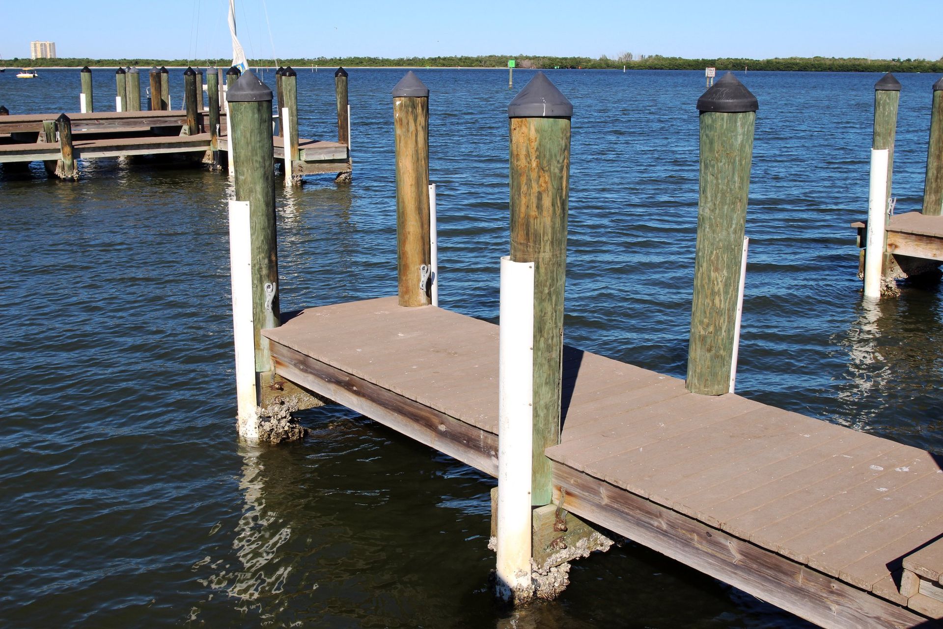 A wooden boat dock with weathered pilings extending into calm blue water on a sunny day.