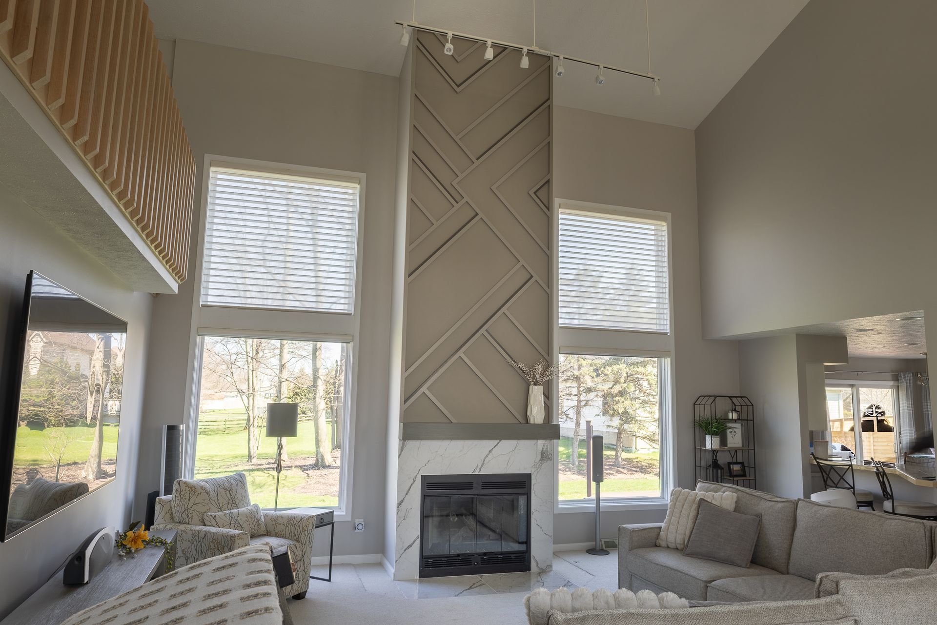 Bright modern living room with tall fireplace, large windows, beige sofas, and patterned accent wall