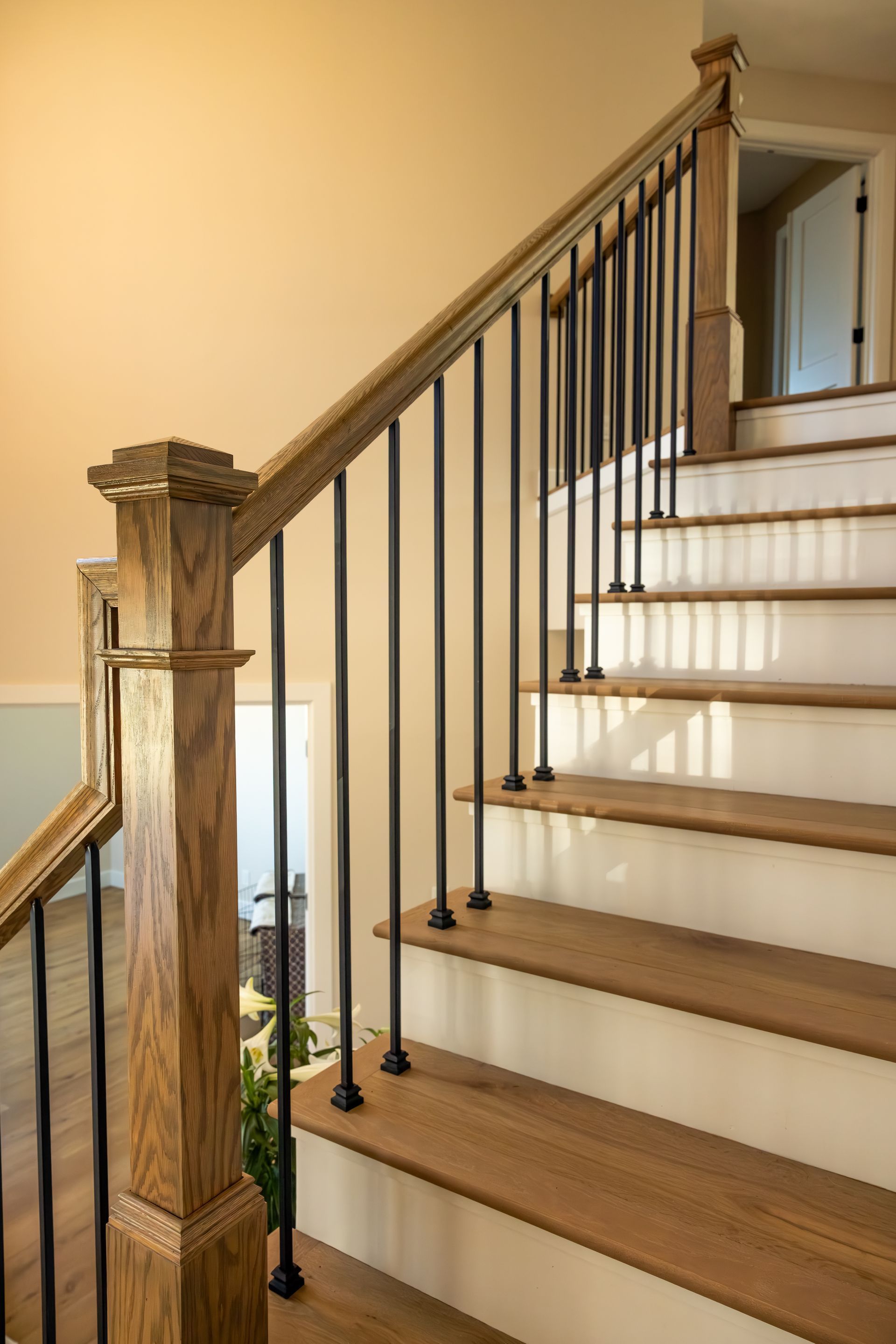 Wooden staircase with white risers, black balusters, and carved wood newel post in a beige interior