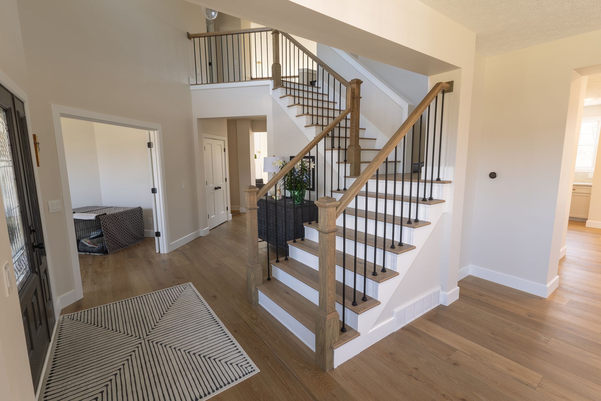 Modern home foyer with staircase, wood floors, and a patterned rug opening to a living area.