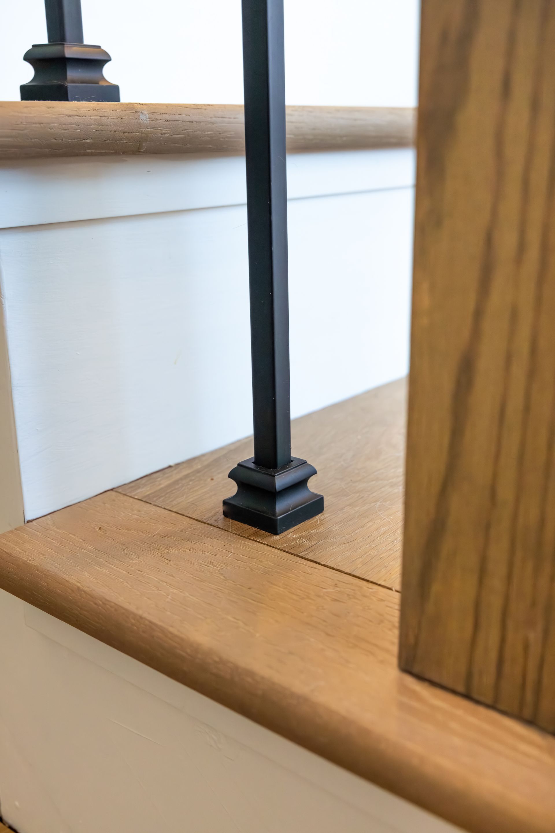 Close-up of a black stair railing post beside a wooden handrail and white trim.