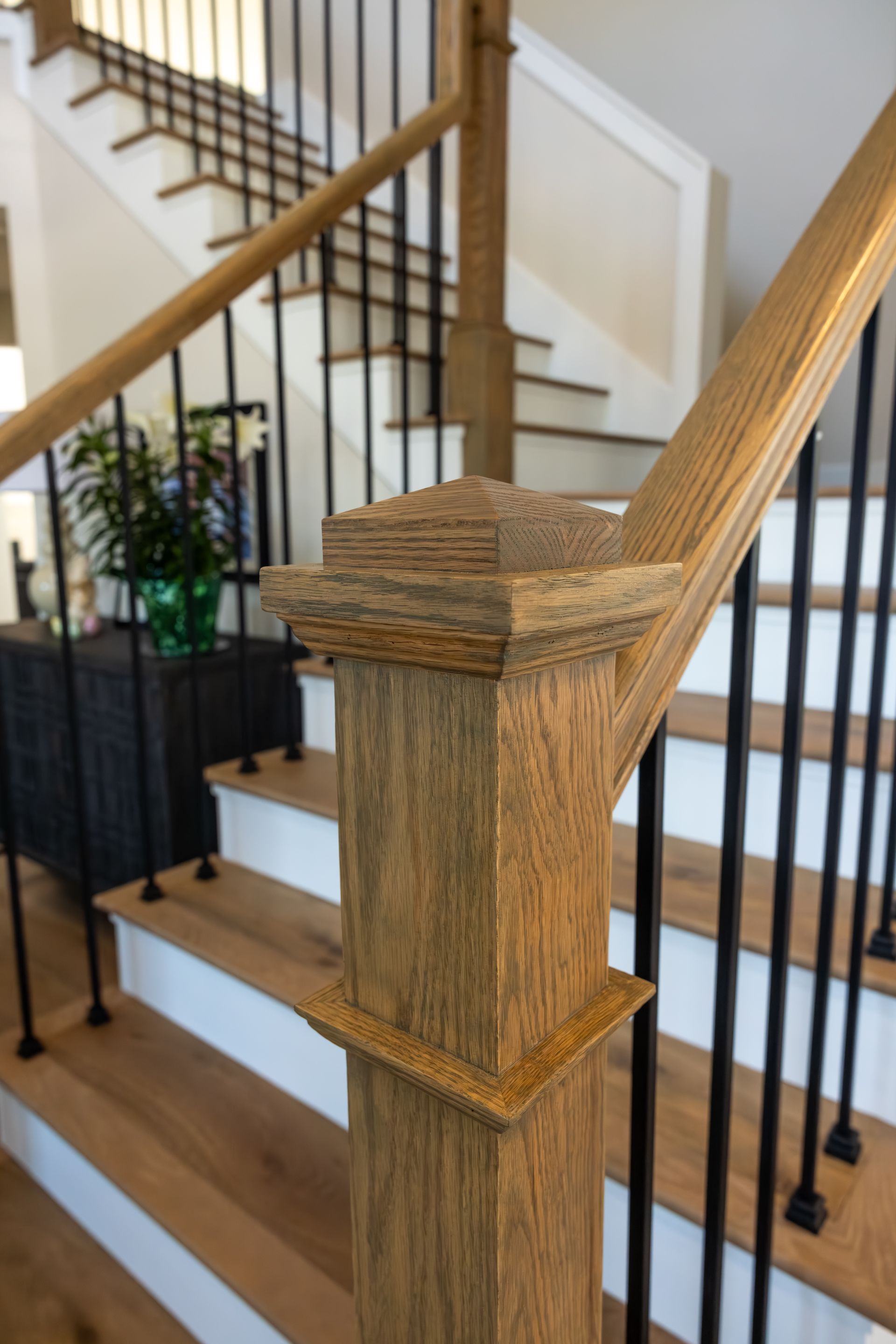 Wooden staircase newel post with black iron balusters in a bright interior foyer
