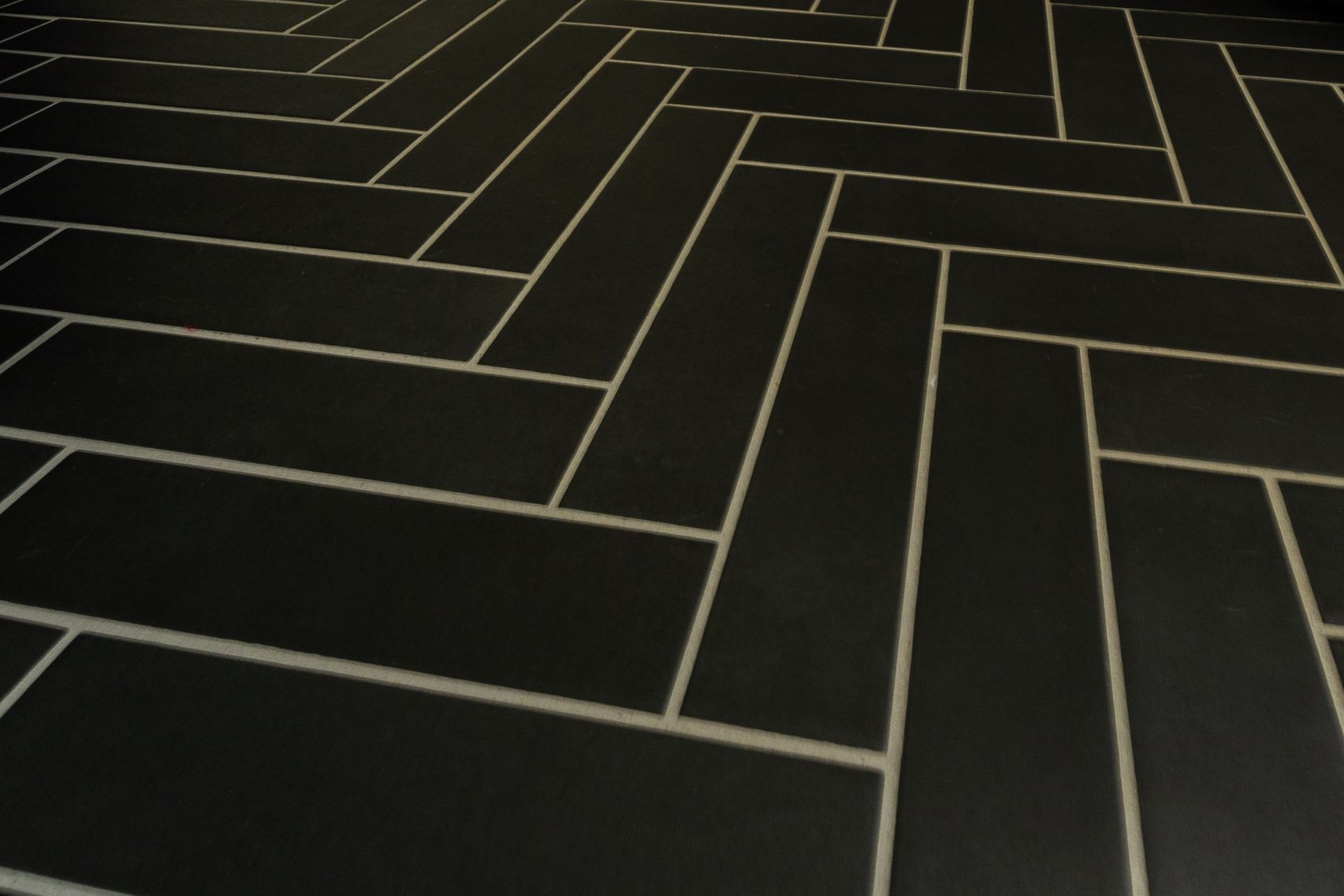Dark geometric tile floor with thin light grout lines forming a herringbone pattern