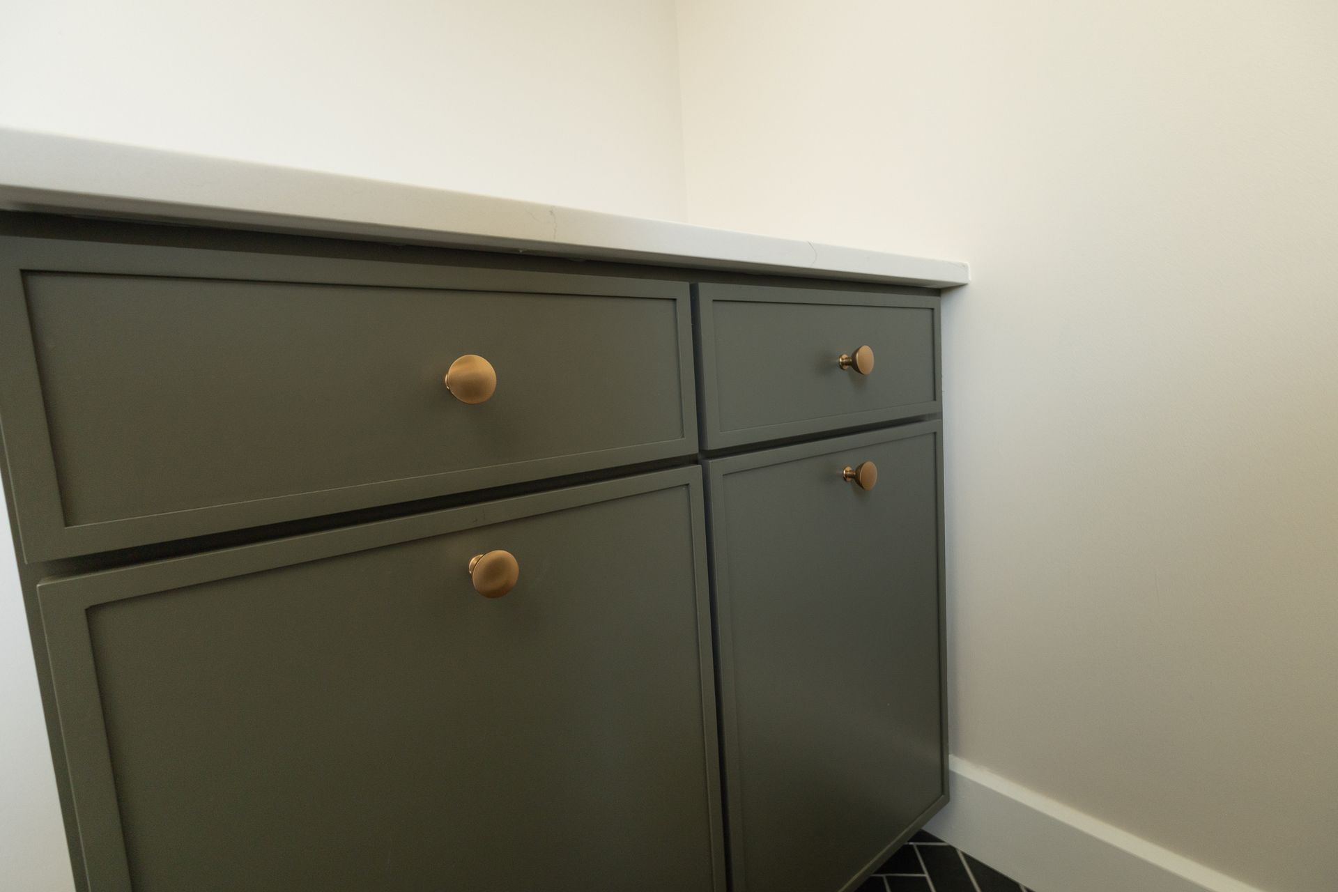 Gray cabinet with brass knobs against a white wall