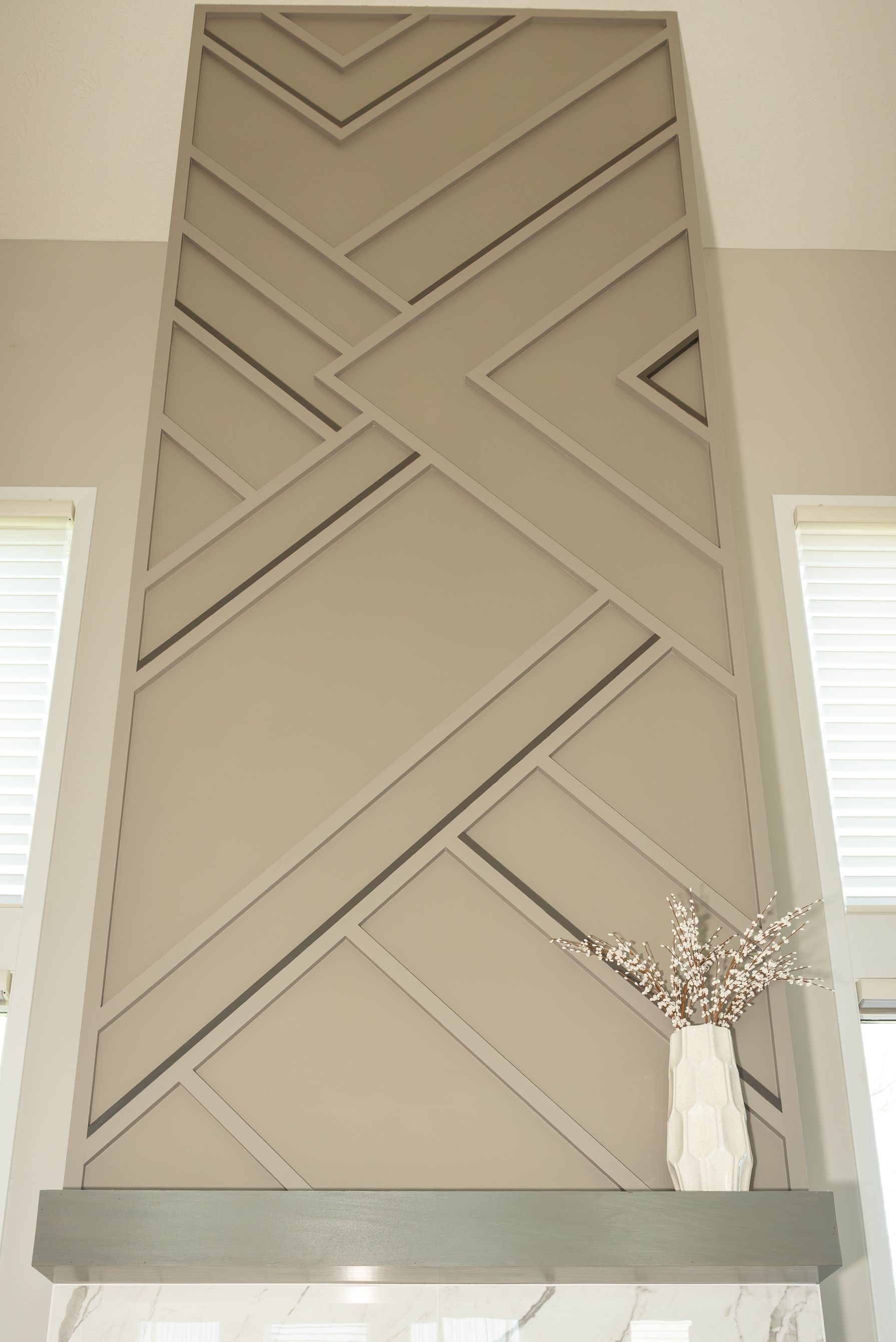Tall beige fireplace with geometric chevron trim and a white mantel in a bright room