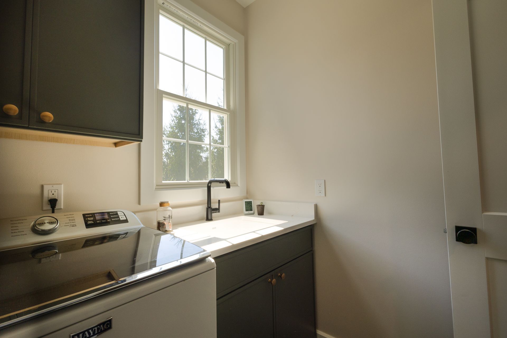 Small kitchen with white sink under a window, dark cabinets, and a stove on the left.