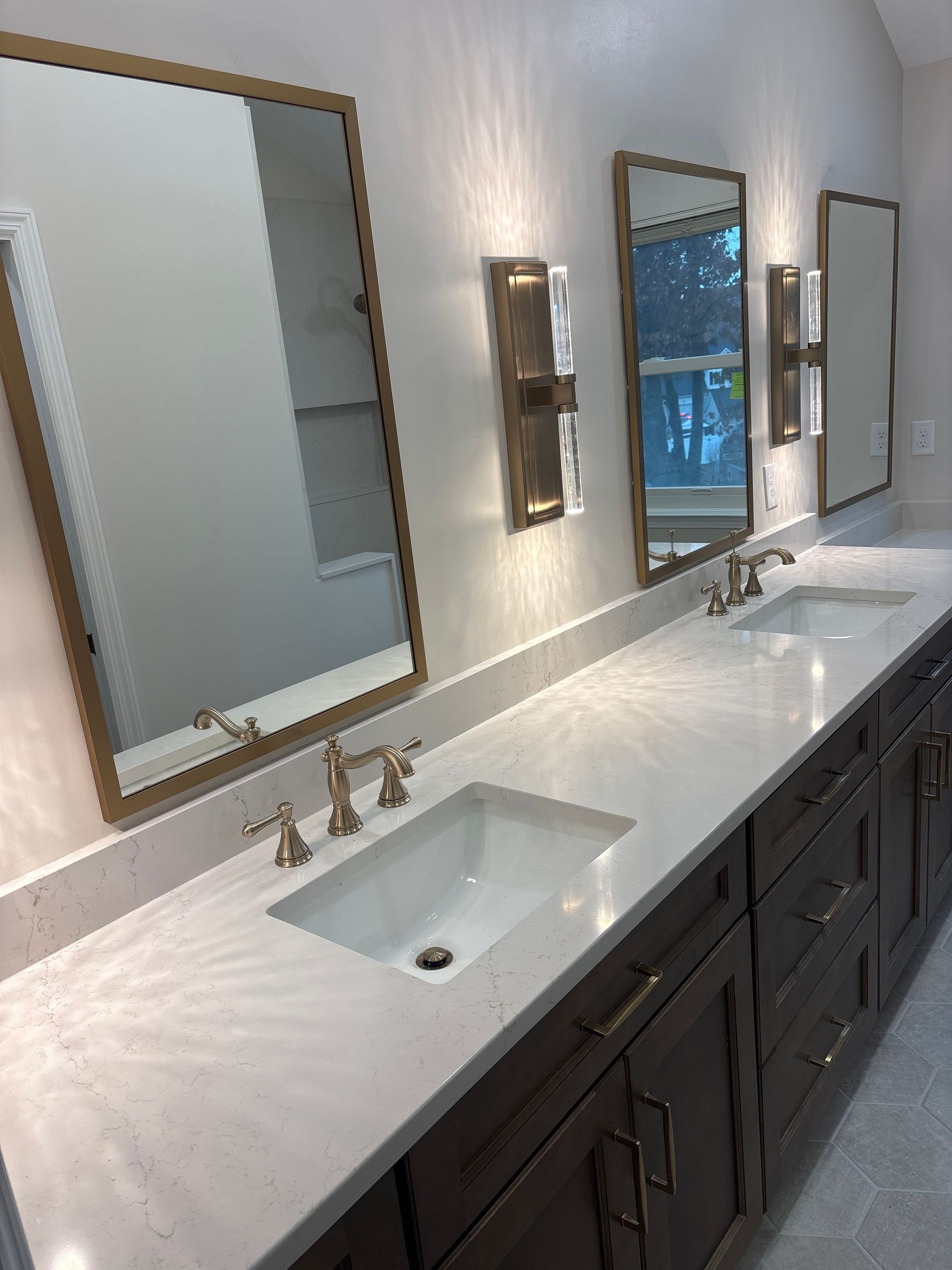 Modern bathroom vanity with two sinks, large mirrors, and dark cabinets against a light wall.
