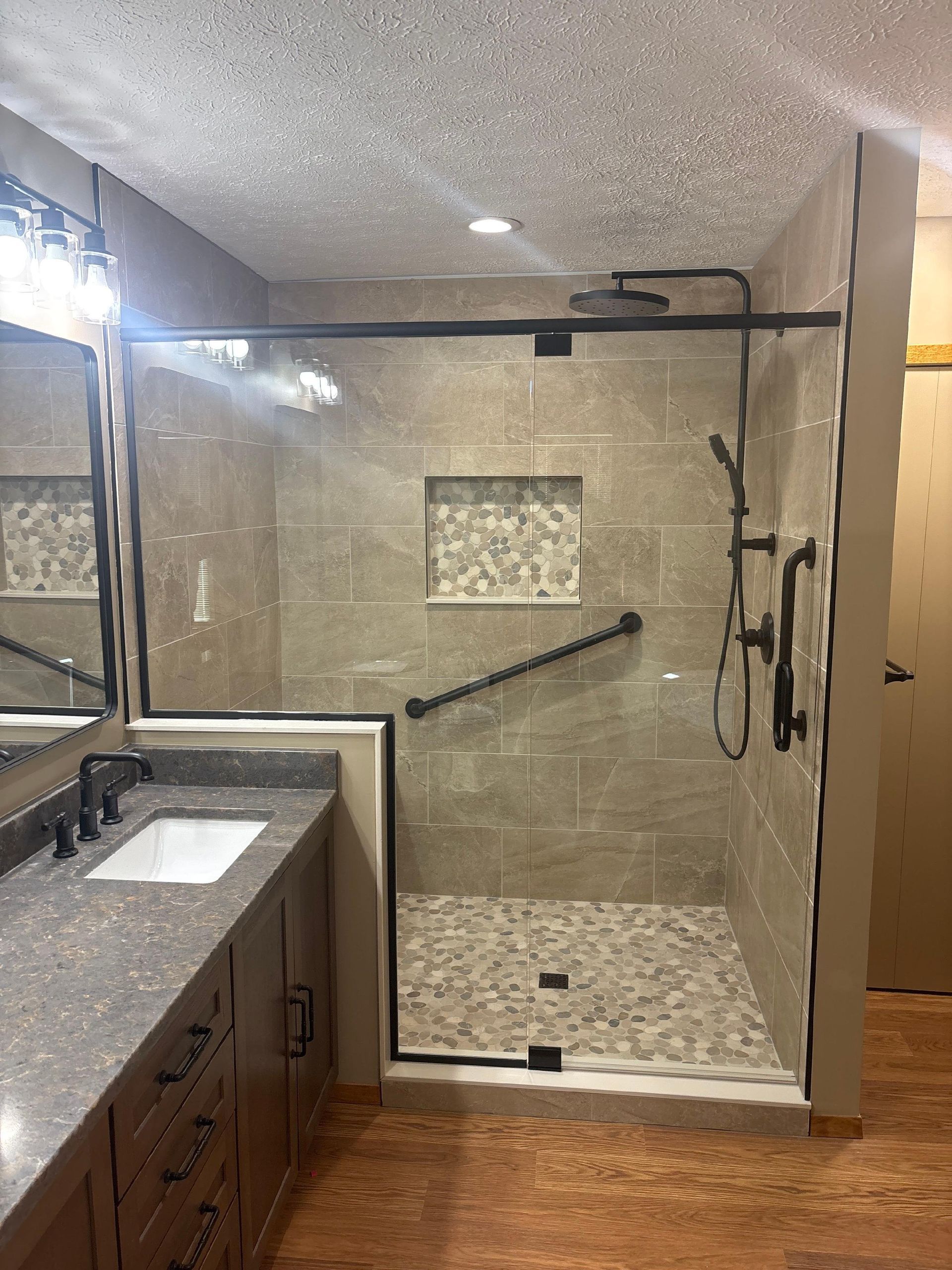 Bathroom with glass walk-in shower, gray tile, black fixtures, and a vanity sink on the left.