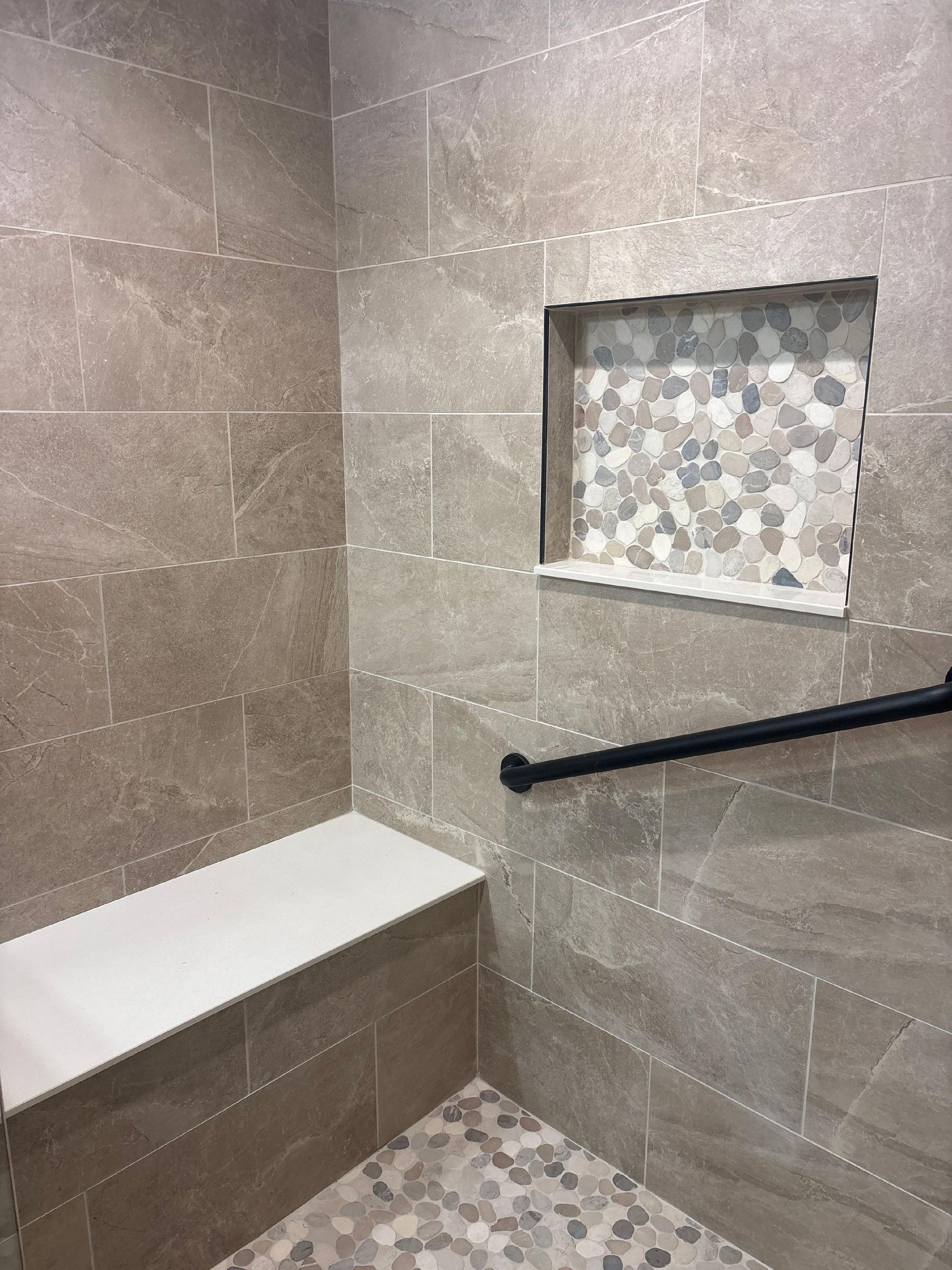 Modern shower with gray tile, built-in bench, recessed shelf, and black grab bar.