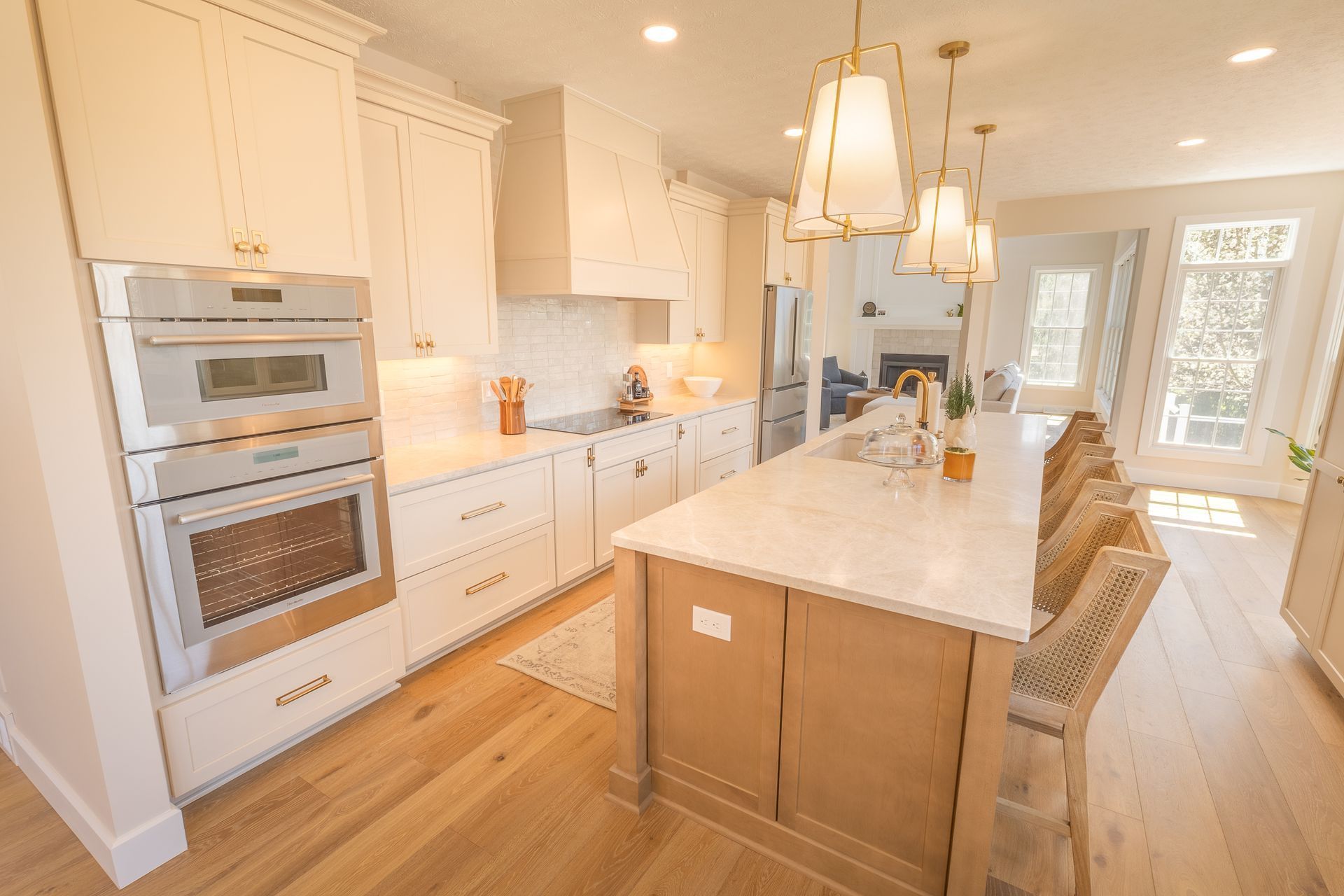 Bright white kitchen with large island, pendant lights, double ovens, and hardwood floors