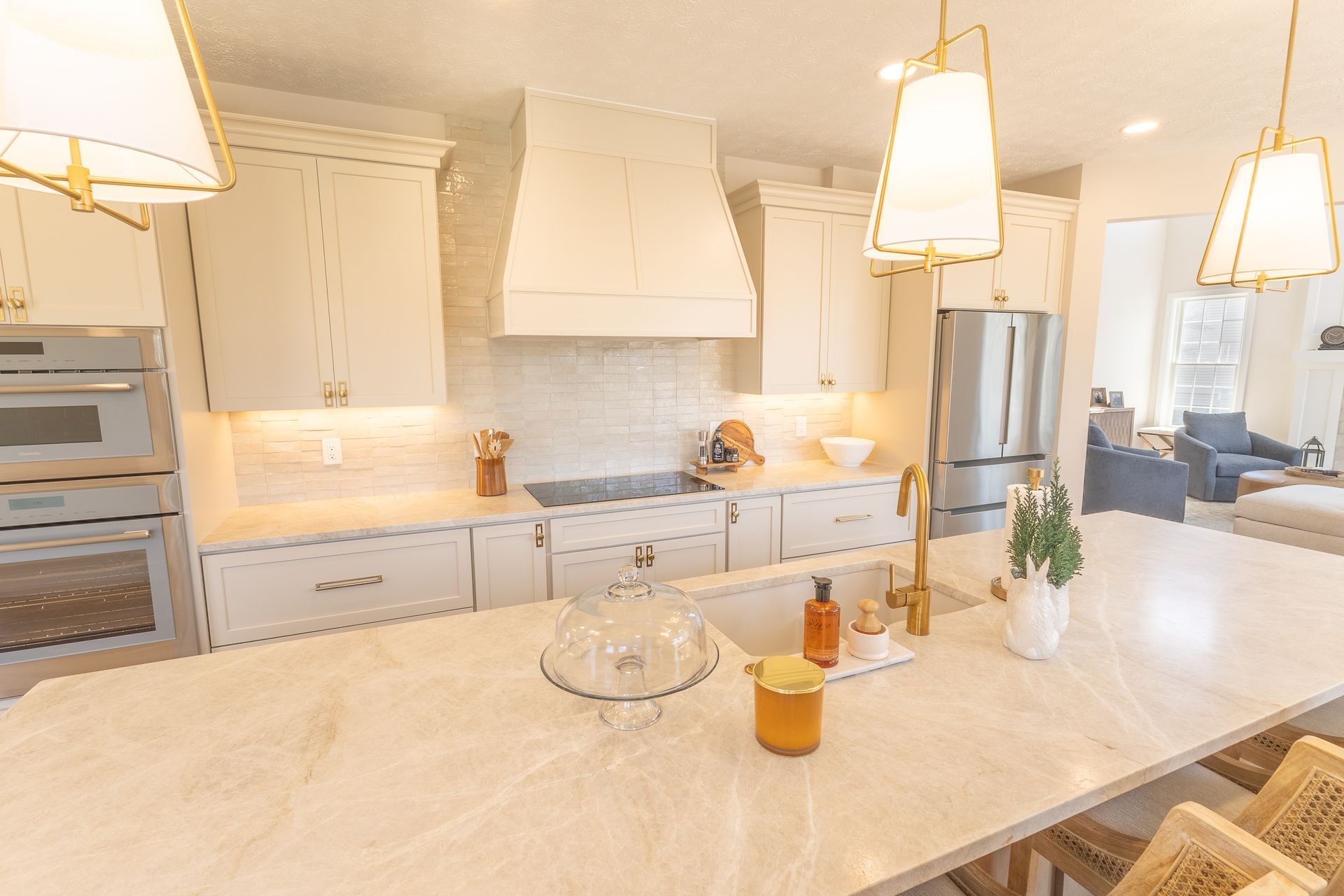 Bright white kitchen with marble island, pendant lights, built-in ovens, and stainless steel fridge