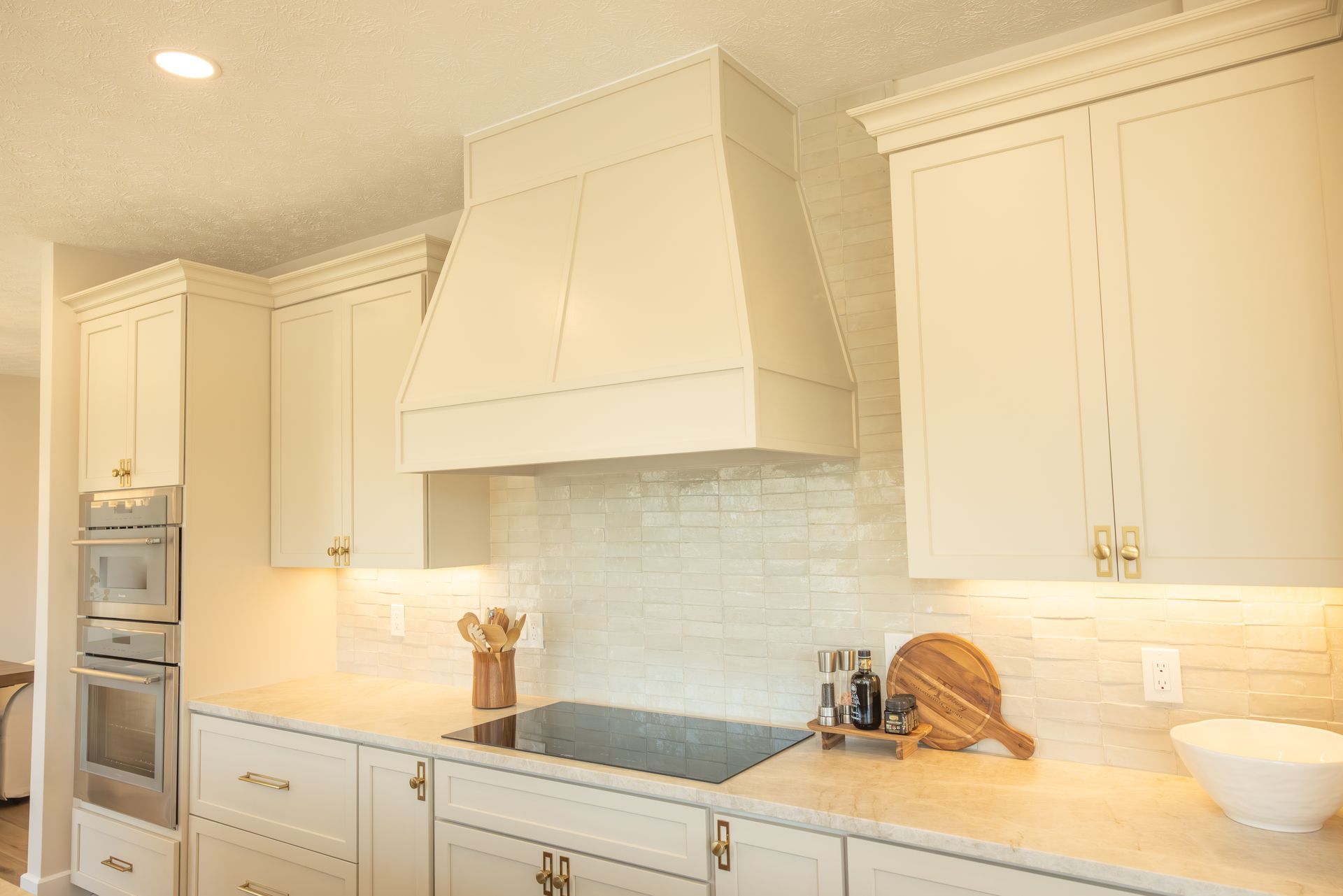 Bright cream kitchen with built-in ovens, stove, white cabinets, and marble countertops