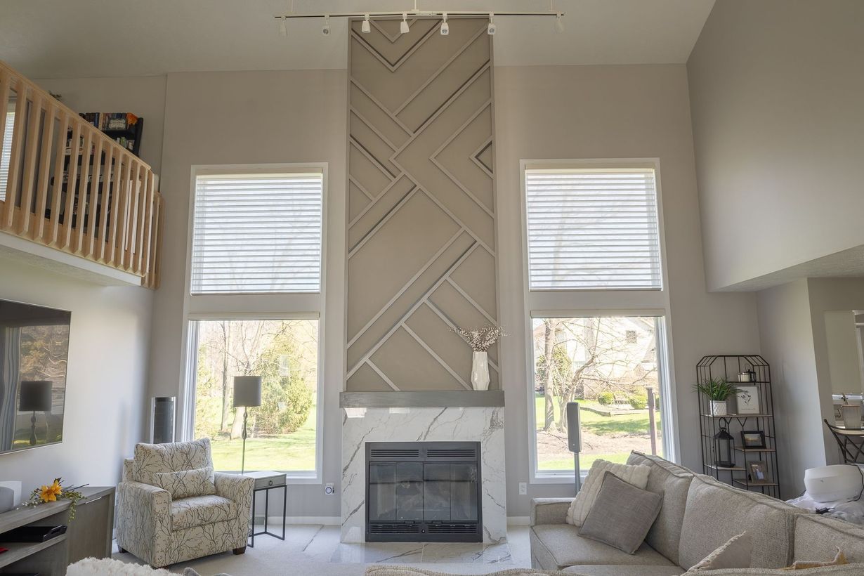 Bright living room with tall windows, vaulted ceiling, fireplace, and neutral sofas