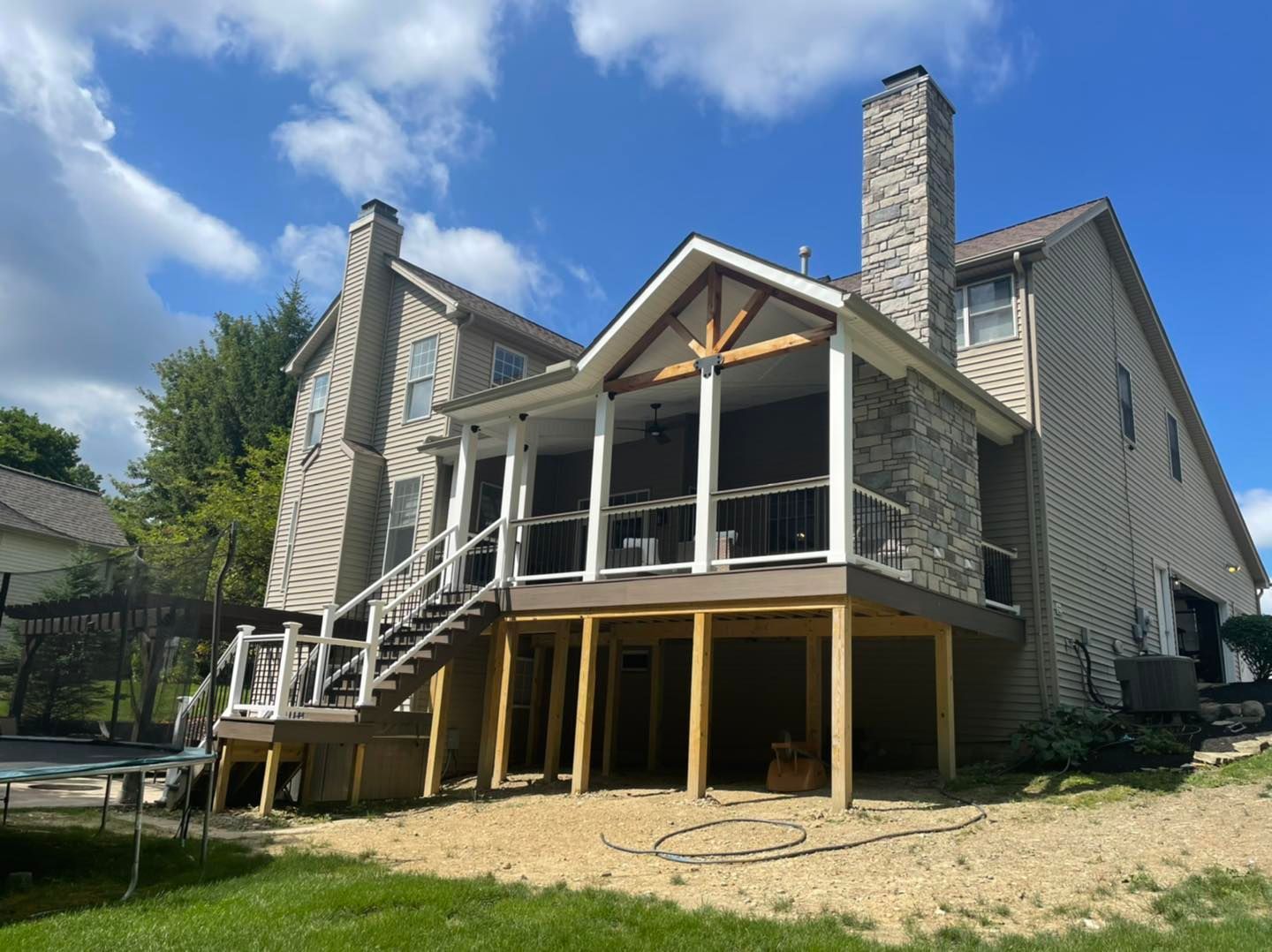 Back of a two-story house with a newly built screened porch and deck, in a sunny backyard setting.