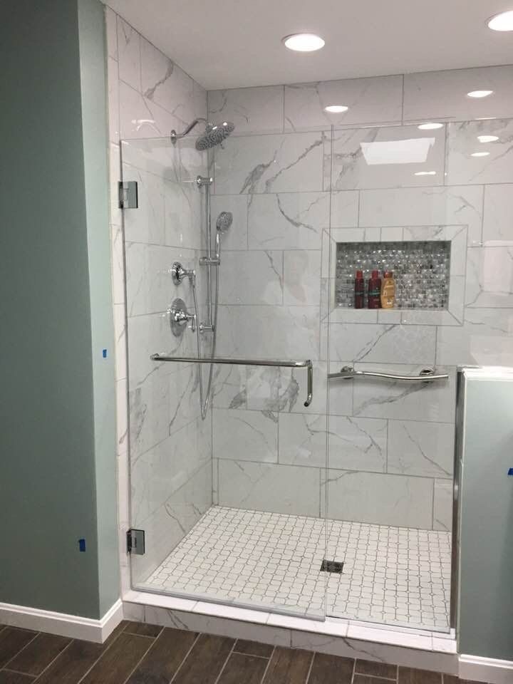 Glass-enclosed shower with marble-look tile. Silver fixtures, recessed shelf, and a tiled floor.