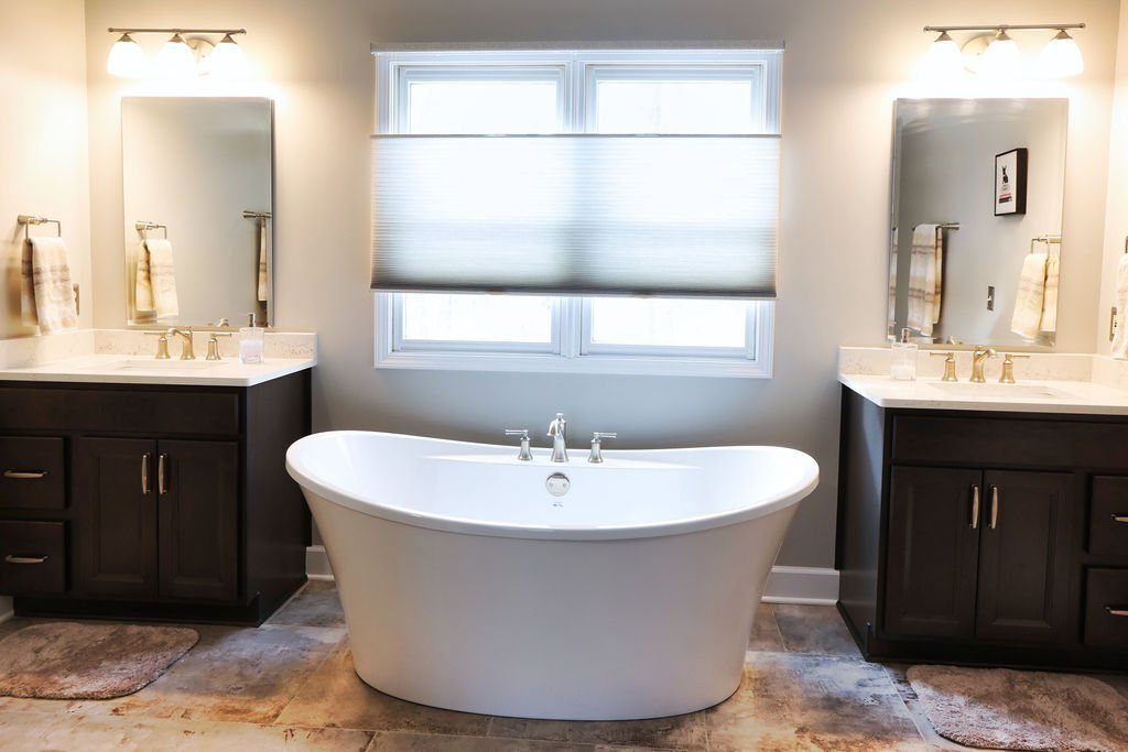 Bathroom with a white freestanding tub, dark brown vanities, and a window.