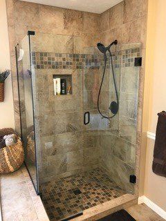 Shower with glass doors and dark hardware, beige and mosaic tile walls, and a dark showerhead.