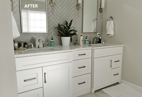 White double vanity bathroom with gray herringbone tile backsplash, two mirrors, and a plant.