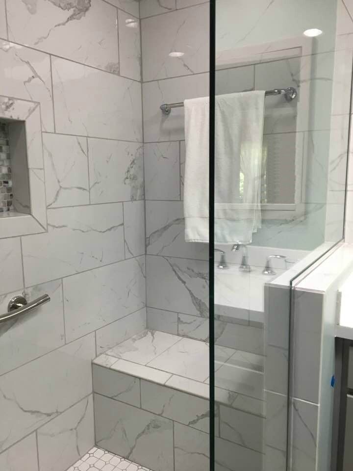 Bathroom with white marble tile shower, glass door, and built-in bench. Towel rack with white towel.
