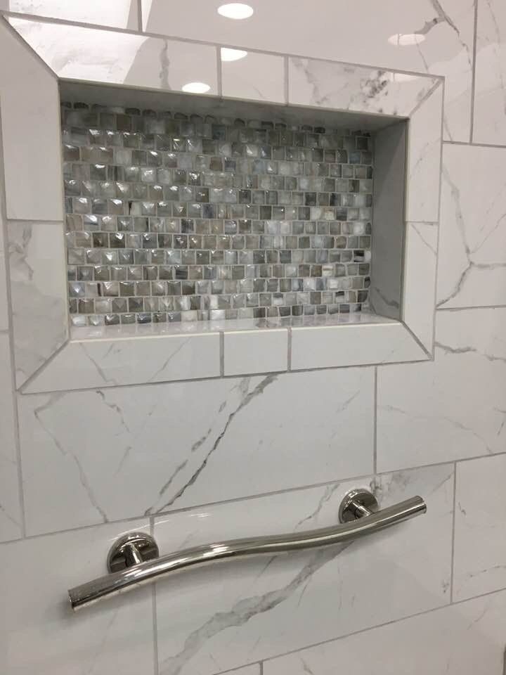 White tile shower with built-in shelf, mosaic tile back, and curved grab bar.