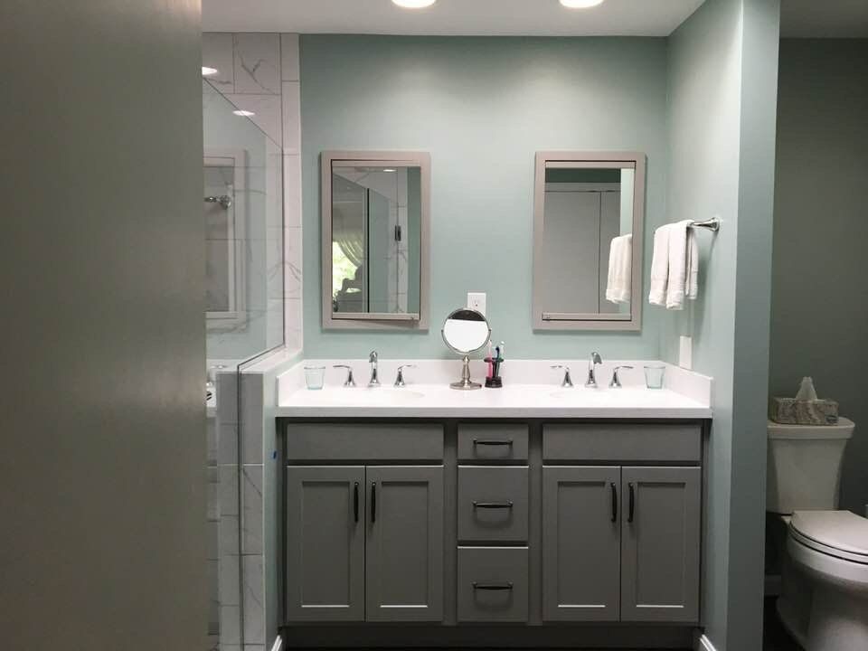 Gray double vanity with mirrors, white countertop, and toilet in a bathroom. Teal walls.