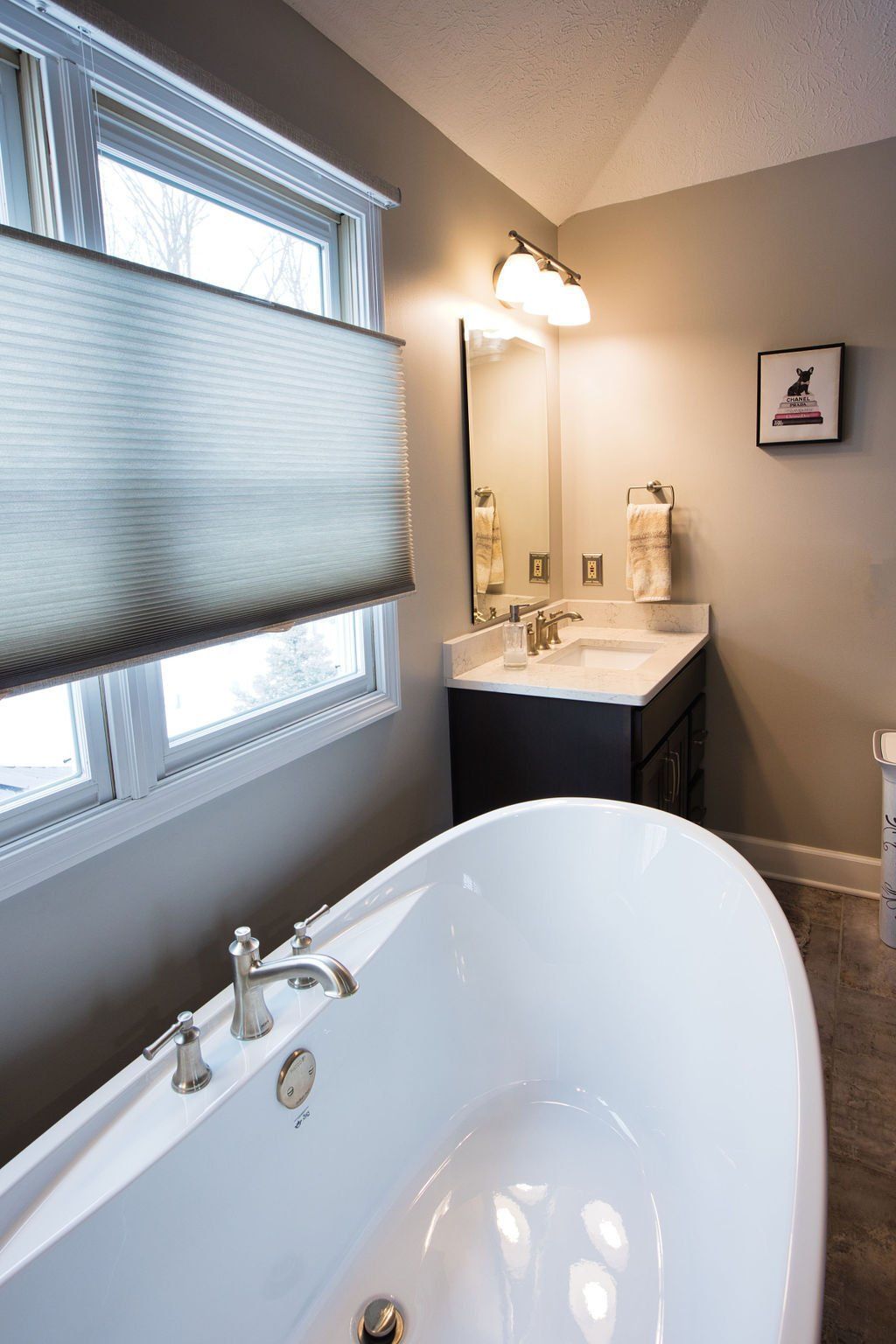 A modern bathroom with a white oval tub, vanity, and window. Gray walls and a neutral color scheme.