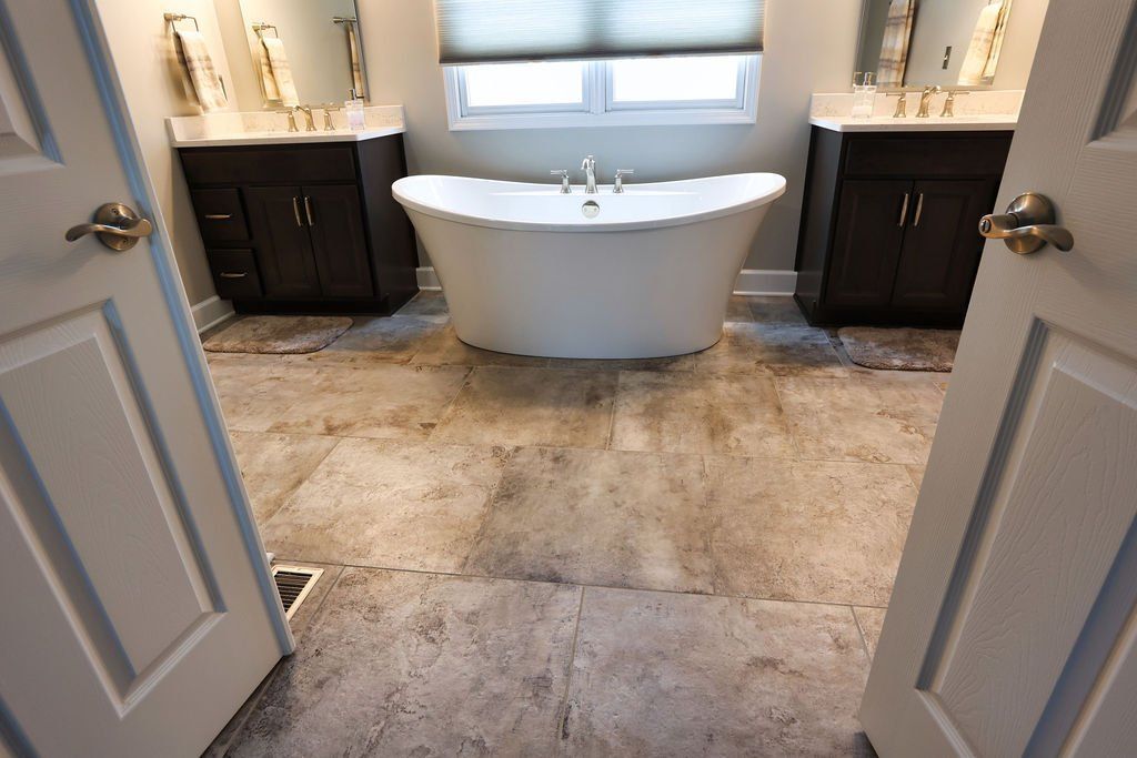 Bathroom with a freestanding tub between two dark vanities and mirrors, open double doors.