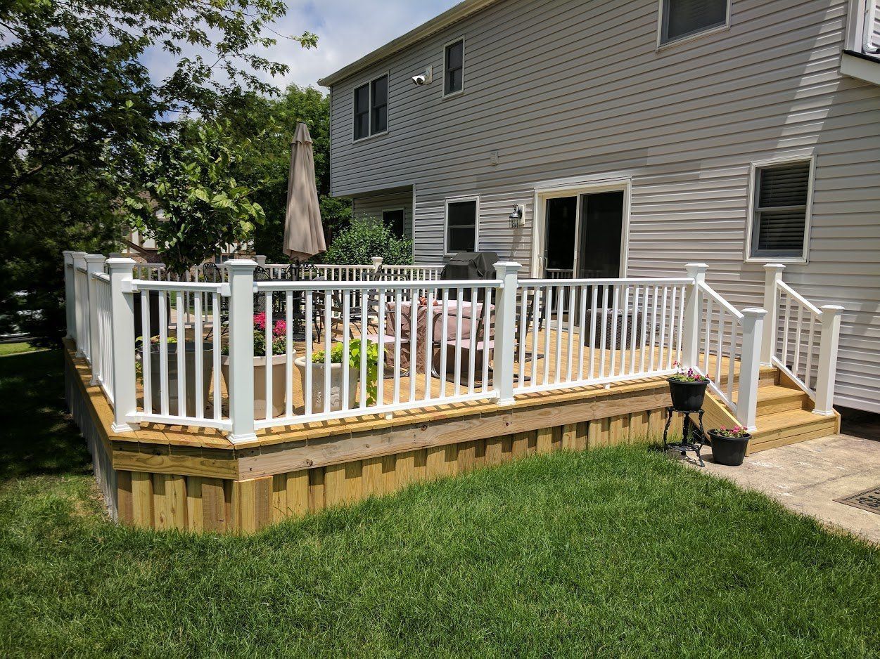 A two-story house with a white-railed deck in the backyard. Deck has steps leading to the ground.