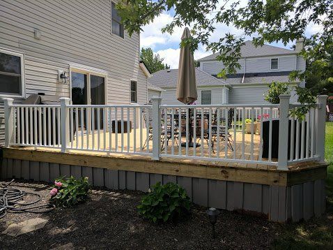 White deck with white railing, grey skirting, and patio furniture next to a house.