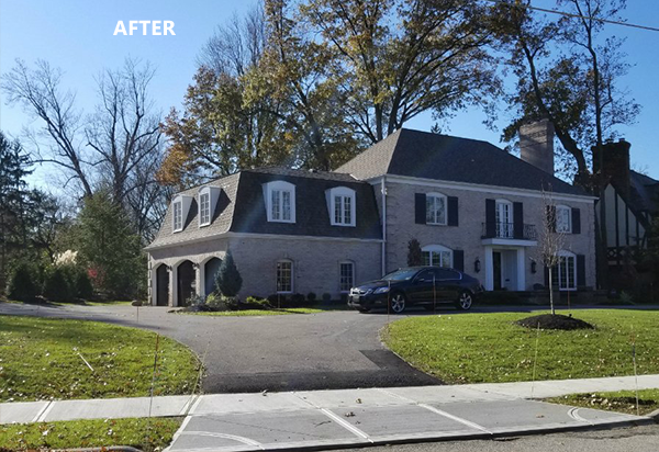 Large brick house with a black car parked in front on a sunny day.