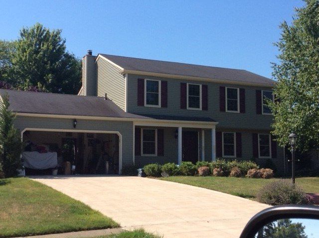 Two-story house with green siding, dark roof, and a driveway; clear blue sky.