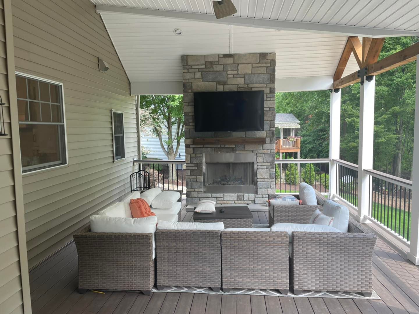 Covered outdoor patio with a stone fireplace, TV, and sectional seating.