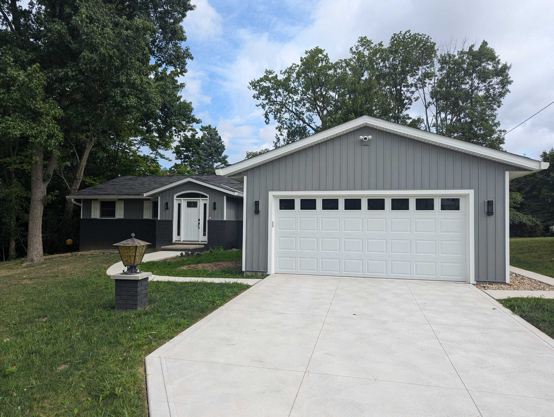 Gray house with white garage door and driveway, situated on a grassy hill.