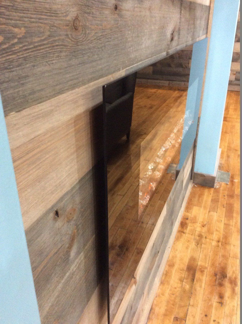 Wood paneled wall with a black appliance and light blue support beams.
