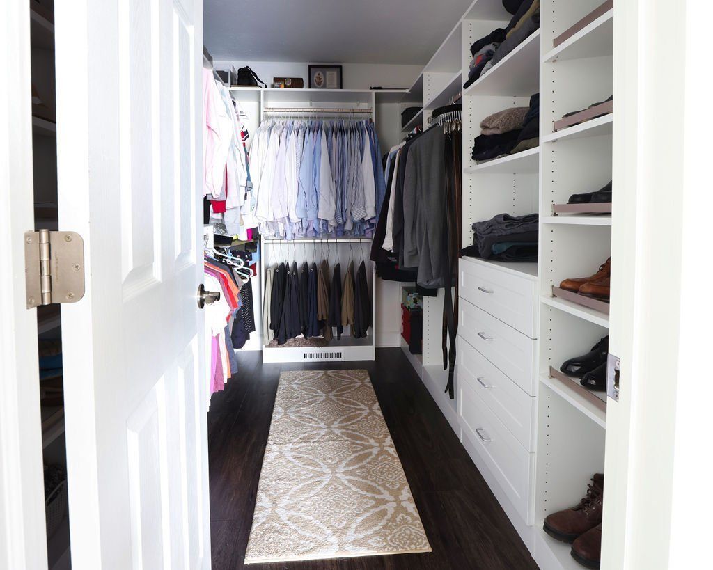 Walk-in closet with white shelves, clothes racks, and a rug. Dark wood floor, doorway on the left.