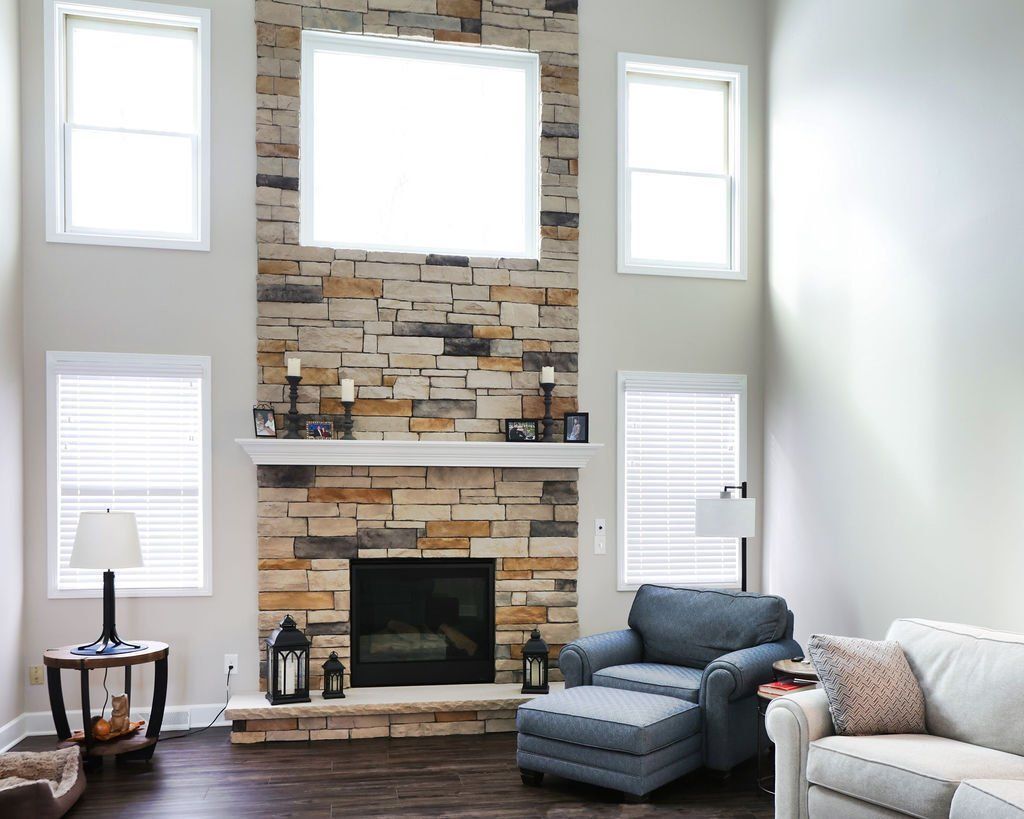 Living room with stone fireplace, windows, blue chair, and white sofa.