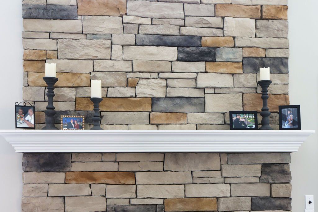 White mantel against a stone wall, decorated with candles and framed photos.