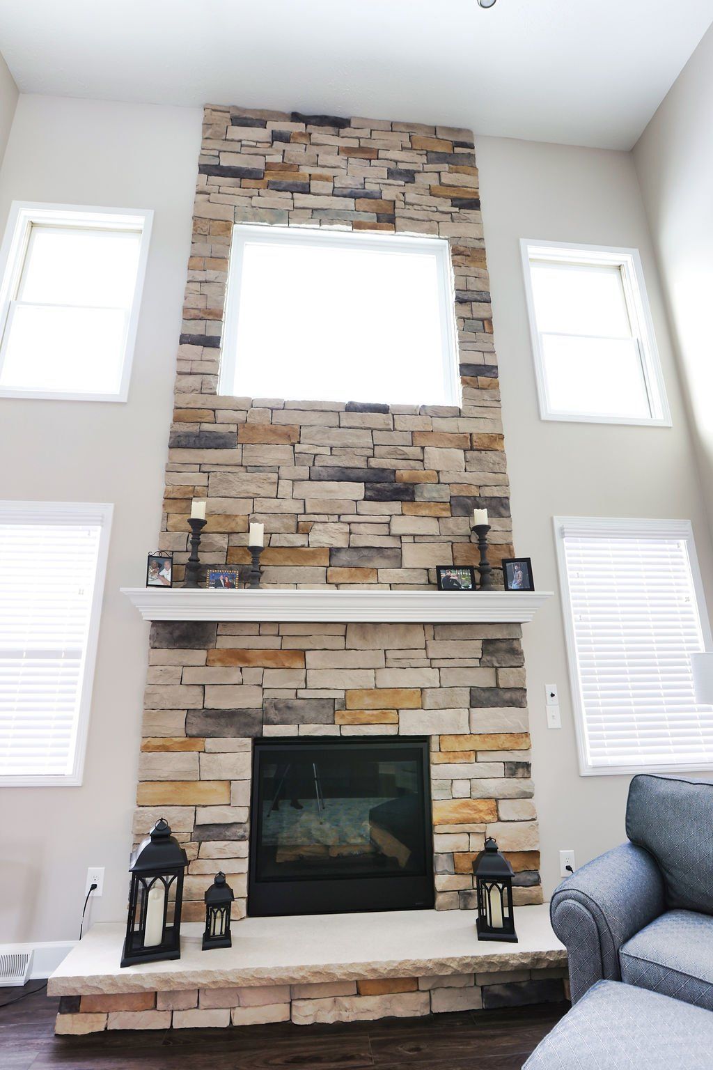 Stone fireplace with a mantel, flanked by windows, in a living room.