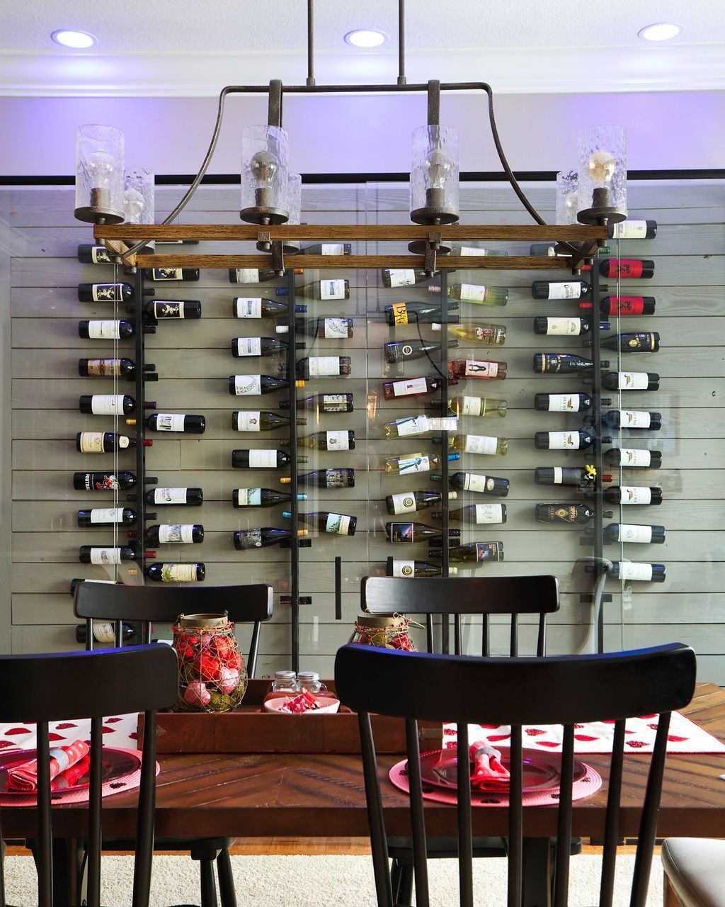 Dining room with wine rack on wall, table set with chairs, overhead lighting.