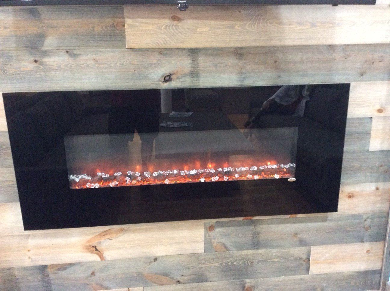 Electric fireplace with black glass frame against a wood-paneled wall; flames visible inside.