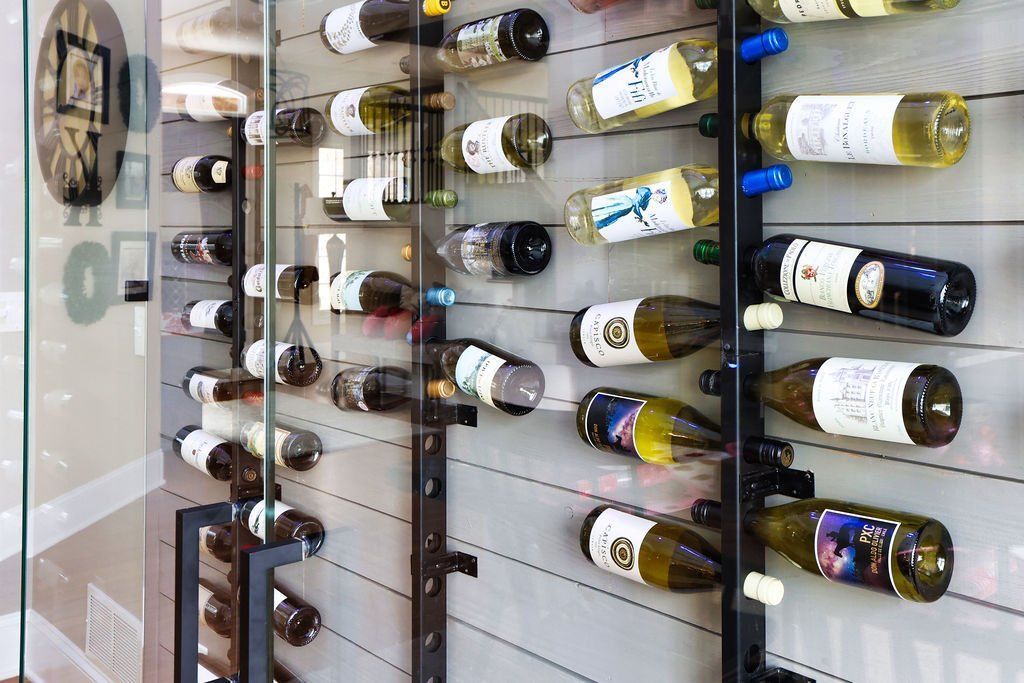 Wine bottles on display in a glass-enclosed, modern wine rack with a neutral-toned wall.