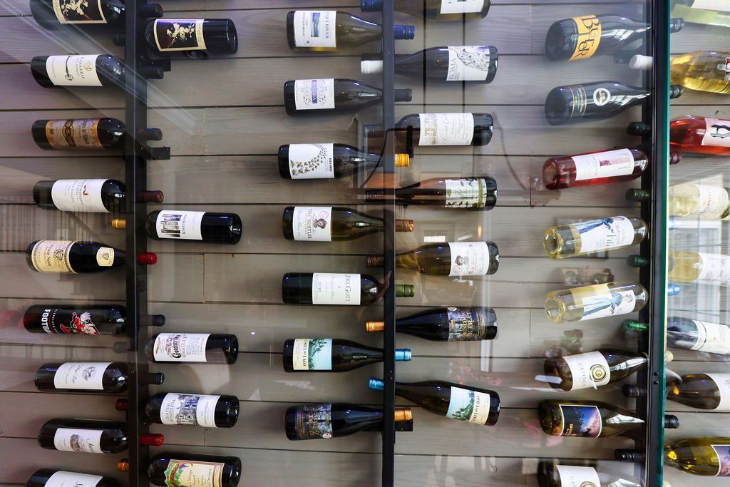 Wine bottles displayed in a glass-fronted rack, various colors and labels visible, store setting.