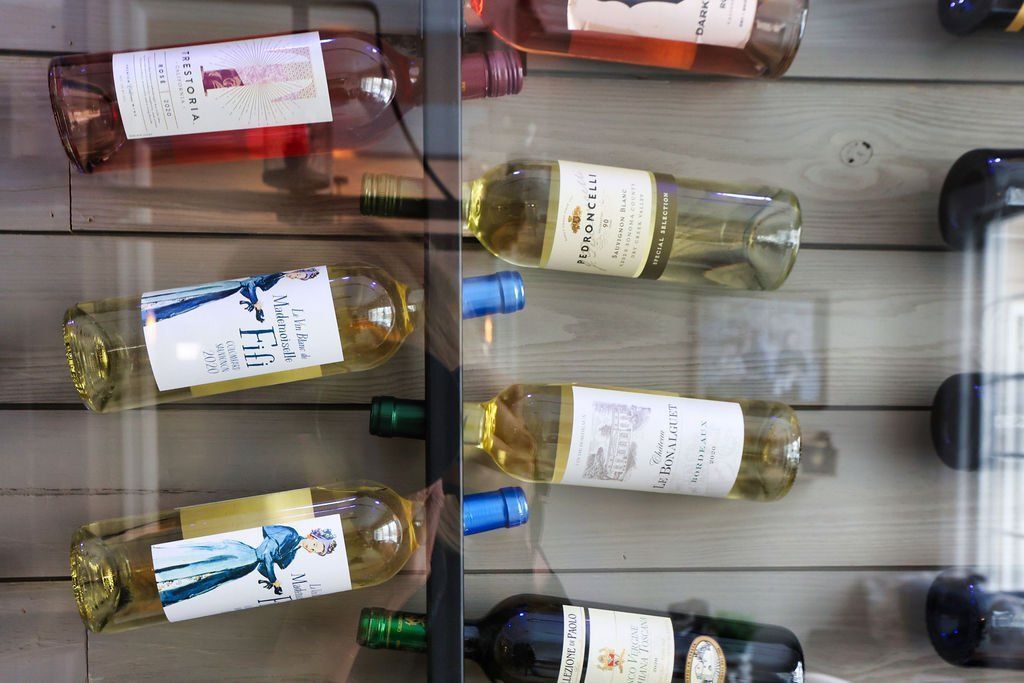 Wine bottles on display in a refrigerated case, with varying colors of wine and label designs.