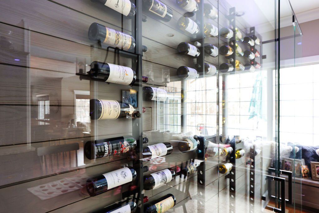 Wine bottles displayed in a modern glass-enclosed storage area, showing off the bottles against a wooden wall.