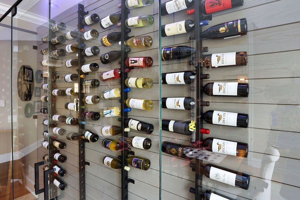Wine bottles displayed on wall-mounted racks behind glass, showing a collection of wines in a modern cellar.